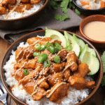 Spicy honey-ginger chicken over white rice, topped with yum yum sauce, sliced avocado, sesame seeds, and green onions in a brown bowl.