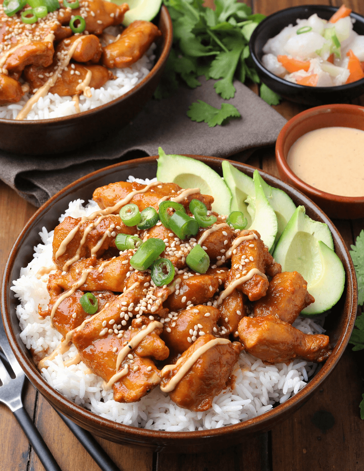 Spicy honey-ginger chicken over white rice, topped with yum yum sauce, sliced avocado, sesame seeds, and green onions in a brown bowl.