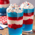 Fourth of July layered jello cups in red, white, and blue, topped with whipped cream and red-blue sprinkles.