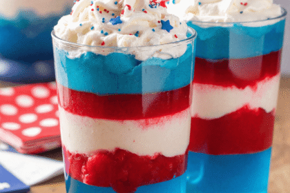 Fourth of July layered jello cups in red, white, and blue, topped with whipped cream and red-blue sprinkles.