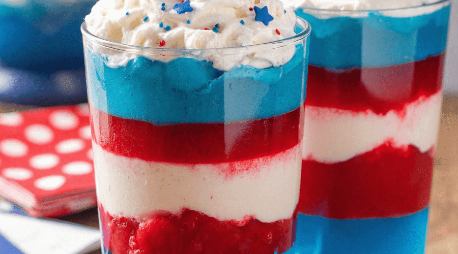 Fourth of July layered jello cups in red, white, and blue, topped with whipped cream and red-blue sprinkles.