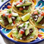 Authentic Mexican Tostadas de Carne Asada topped with grilled steak, avocado slices, shredded lettuce, and queso fresco on a vibrant plate.