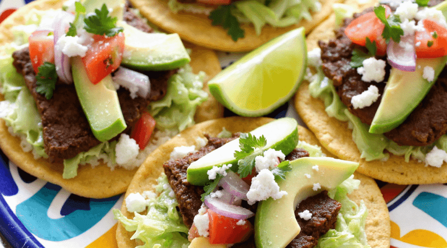 Authentic Mexican Tostadas de Carne Asada topped with grilled steak, avocado slices, shredded lettuce, and queso fresco on a vibrant plate.