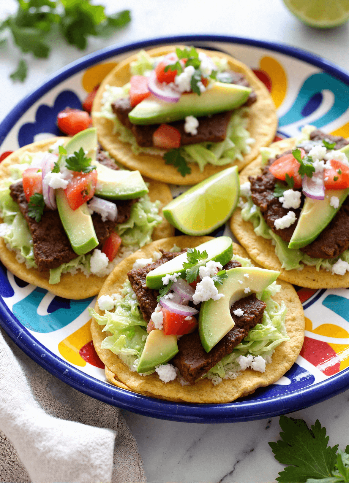 Authentic Mexican Tostadas de Carne Asada topped with grilled steak, avocado slices, shredded lettuce, and queso fresco on a vibrant plate.