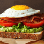 Fried egg BLT avocado toast on whole grain bread with crispy bacon, lettuce, tomato, and smashed avocado.