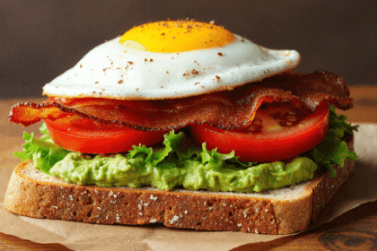 Fried egg BLT avocado toast on whole grain bread with crispy bacon, lettuce, tomato, and smashed avocado.
