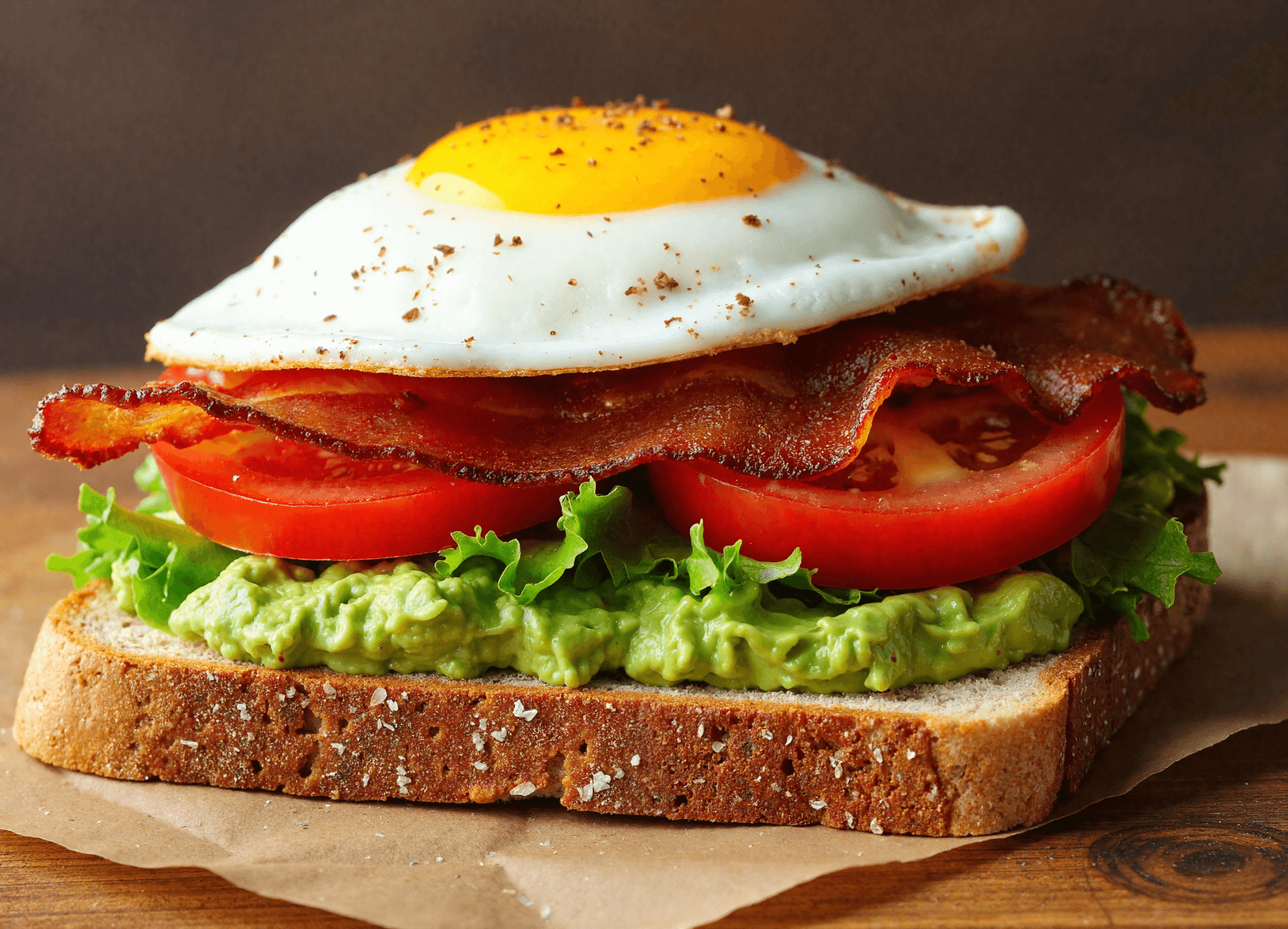 Fried egg BLT avocado toast on whole grain bread with crispy bacon, lettuce, tomato, and smashed avocado.