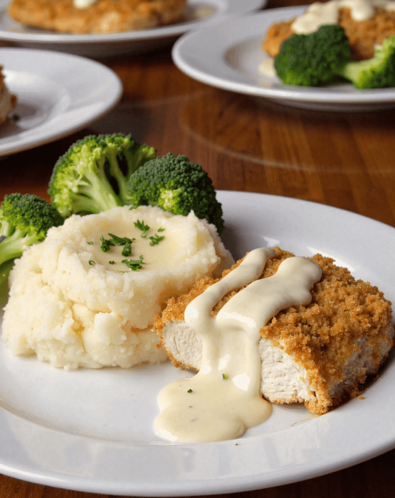 Sliced Longhorn Parmesan Chicken with creamy ranch sauce, served with mashed potatoes and steamed broccoli on a white dinner plate.