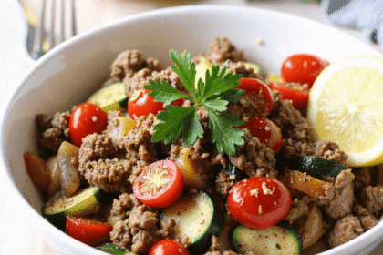Close-up angled view of a white bowl filled with seasoned ground beef, zucchini, tomatoes, and bell peppers garnished with parsley and lemon—ideal for a low-carb Mediterranean dinner.