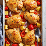 Baked Hawaiian chicken thighs with pineapple, red bell pepper, grape tomatoes, and onion on a sheet pan