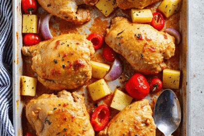 Baked Hawaiian chicken thighs with pineapple, red bell pepper, grape tomatoes, and onion on a sheet pan