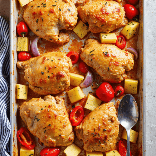 Baked Hawaiian chicken thighs with pineapple, red bell pepper, grape tomatoes, and onion on a sheet pan