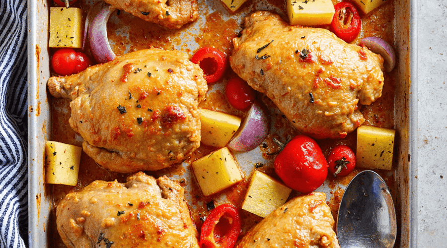 Baked Hawaiian chicken thighs with pineapple, red bell pepper, grape tomatoes, and onion on a sheet pan