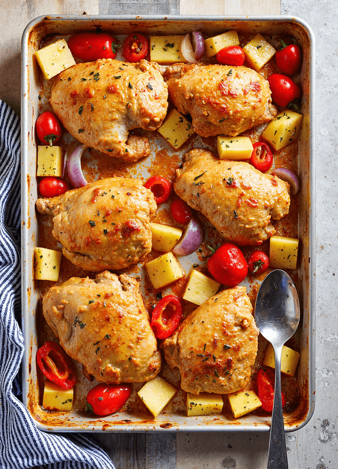 Baked Hawaiian chicken thighs with pineapple, red bell pepper, grape tomatoes, and onion on a sheet pan