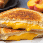 Close-up of honey peach white cheddar grilled cheese sandwich with melted cheese and sliced peach between crispy golden toasted bread.