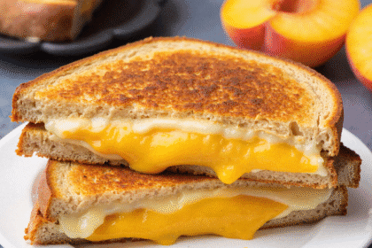 Close-up of honey peach white cheddar grilled cheese sandwich with melted cheese and sliced peach between crispy golden toasted bread.