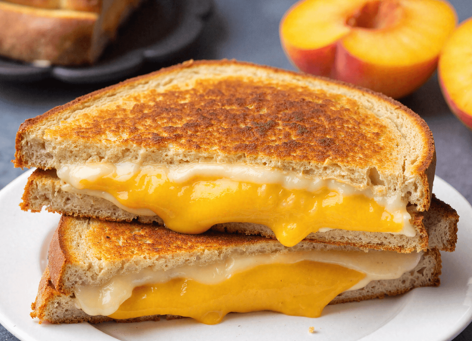 Close-up of honey peach white cheddar grilled cheese sandwich with melted cheese and sliced peach between crispy golden toasted bread.