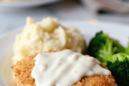Close-up of crispy Longhorn Steakhouse Parmesan Chicken topped with creamy ranch cheese sauce, served with mashed potatoes and steamed broccoli on a white plate.