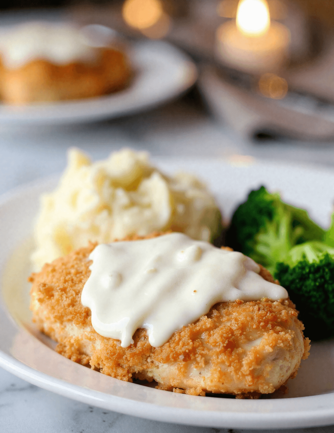 Close-up of crispy Longhorn Steakhouse Parmesan Chicken topped with creamy ranch cheese sauce, served with mashed potatoes and steamed broccoli on a white plate.