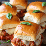 Tray of mini meatball parmesan sliders with marinara, mozzarella, and basil leaves on golden buns.
