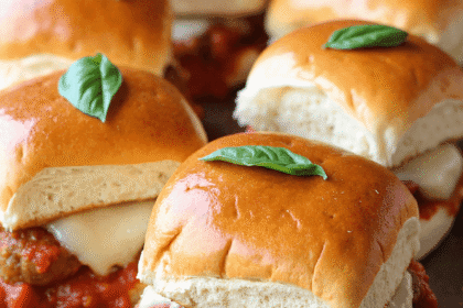 Tray of mini meatball parmesan sliders with marinara, mozzarella, and basil leaves on golden buns.