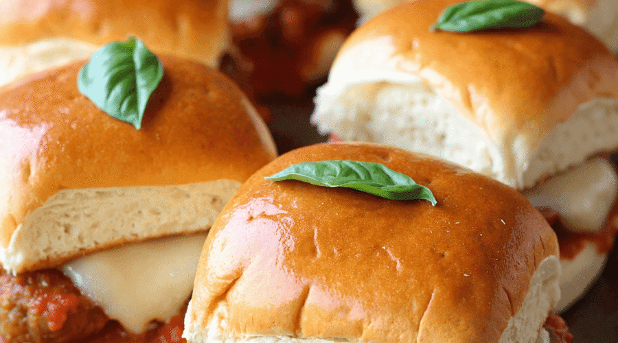 Tray of mini meatball parmesan sliders with marinara, mozzarella, and basil leaves on golden buns.