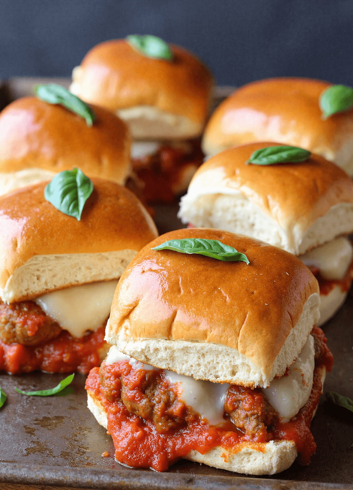Tray of mini meatball parmesan sliders with marinara, mozzarella, and basil leaves on golden buns.