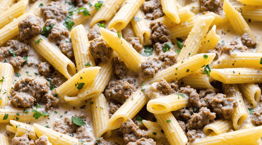 One-pot penne pasta with creamy ground beef sauce in a skillet, garnished with parsley.
