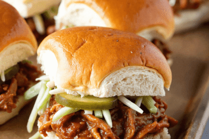 Close-up of pulled pork BBQ sliders on soft golden buns with pickles and slaw