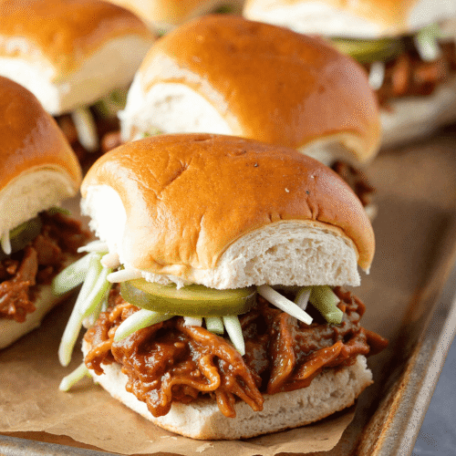 Close-up of pulled pork BBQ sliders on soft golden buns with pickles and slaw