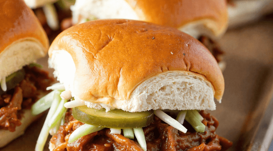 Close-up of pulled pork BBQ sliders on soft golden buns with pickles and slaw