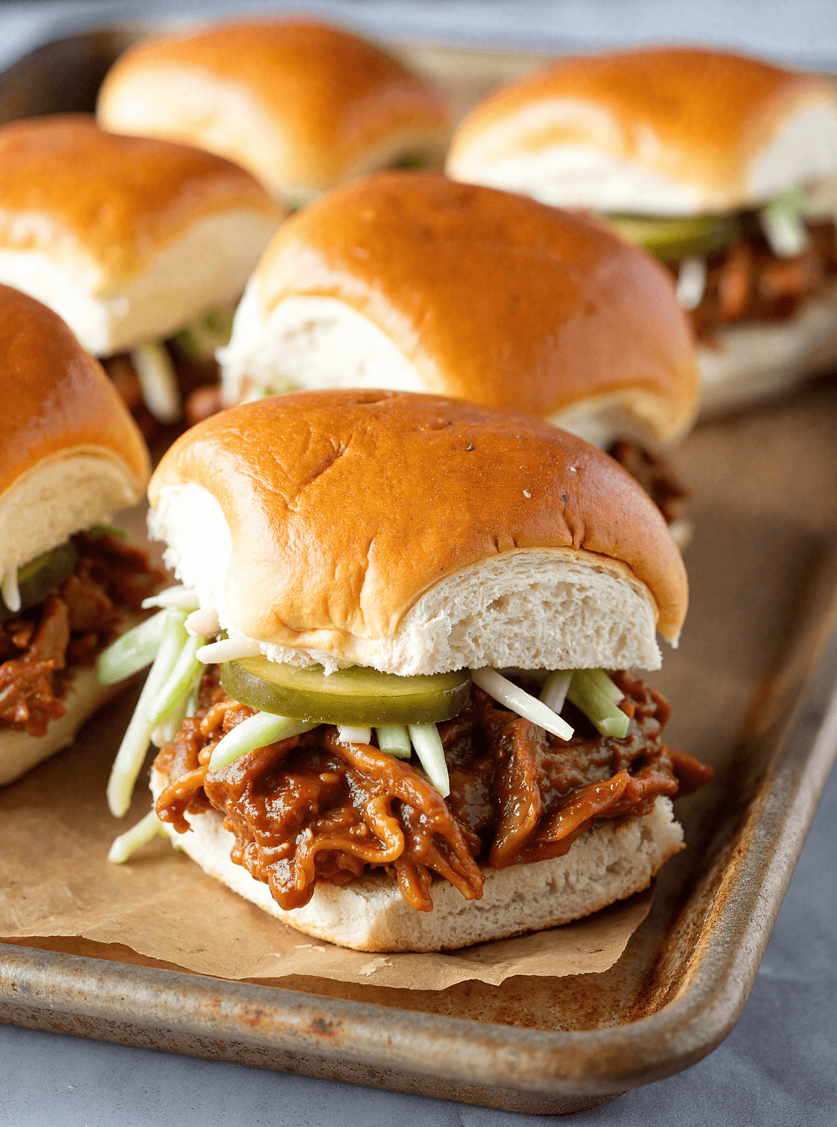 Close-up of pulled pork BBQ sliders on soft golden buns with pickles and slaw