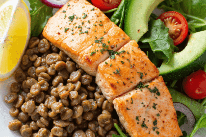 Healthy salmon and lentil salad bowl with leafy greens, cherry tomatoes, avocado slices, lemon wedge, and seasoned grilled salmon.
