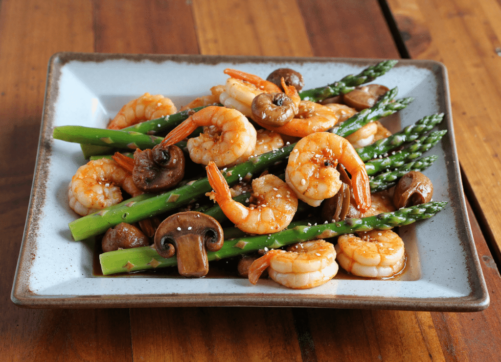 Stir-fried shrimp, asparagus, and mushrooms served on a ceramic plate with a glossy garlic soy sauce.
