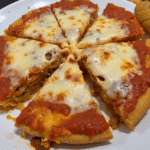 Overhead view of a sliced spaghetti pie on a white plate, with melted cheese and rich tomato sauce baked over a golden pasta crust, ready for family dinner.