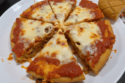 Overhead view of a sliced spaghetti pie on a white plate, with melted cheese and rich tomato sauce baked over a golden pasta crust, ready for family dinner.