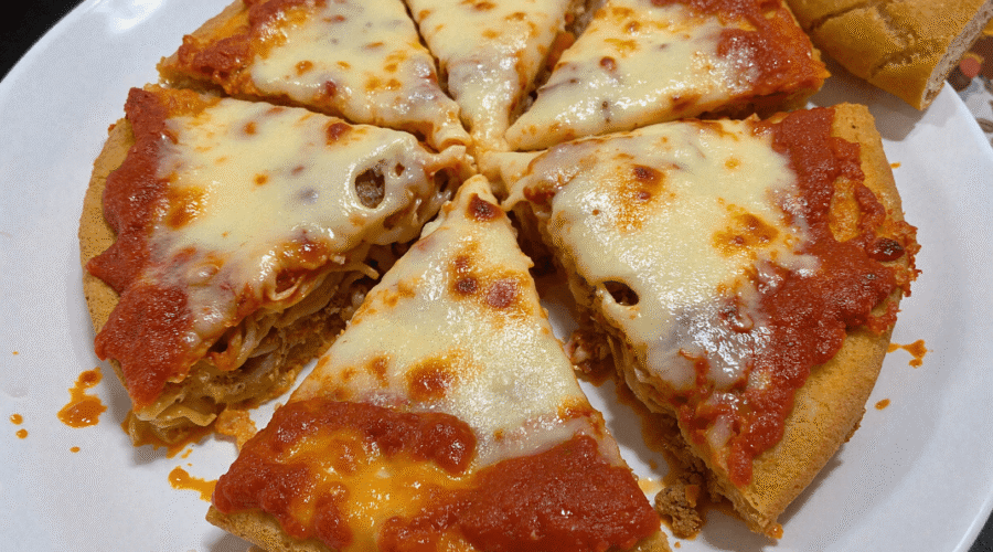 Overhead view of a sliced spaghetti pie on a white plate, with melted cheese and rich tomato sauce baked over a golden pasta crust, ready for family dinner.