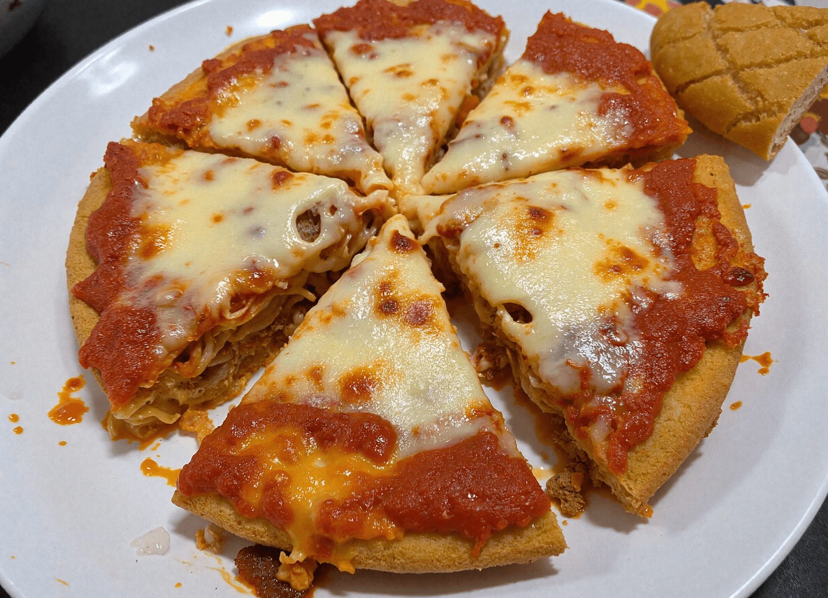 Overhead view of a sliced spaghetti pie on a white plate, with melted cheese and rich tomato sauce baked over a golden pasta crust, ready for family dinner.