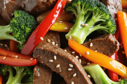 Sliced beef stir-fry with broccoli, red and yellow peppers, served over white rice and topped with sesame seeds.