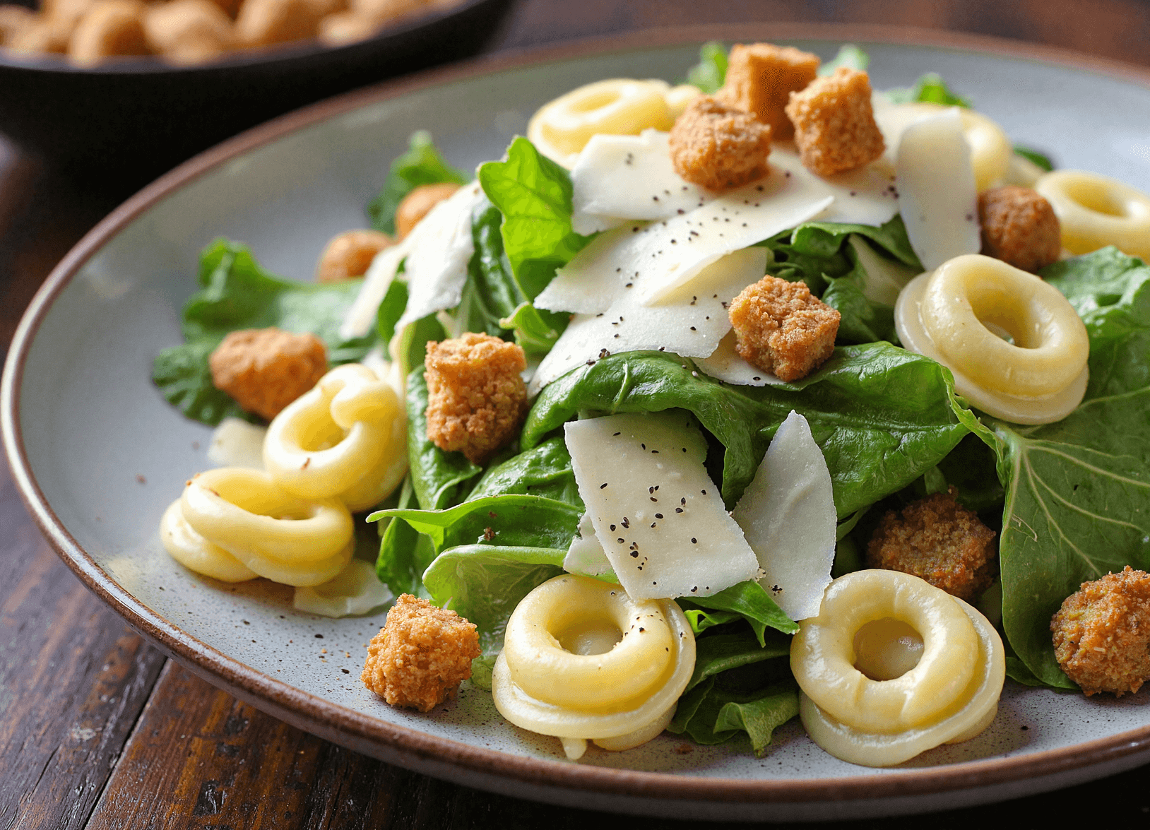 Cheese tortellini Caesar salad served on a ceramic plate with romaine, shaved parmesan, and croutons.