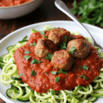 Baked turkey meatballs served over spiralized zucchini noodles and marinara sauce, garnished with parsley.