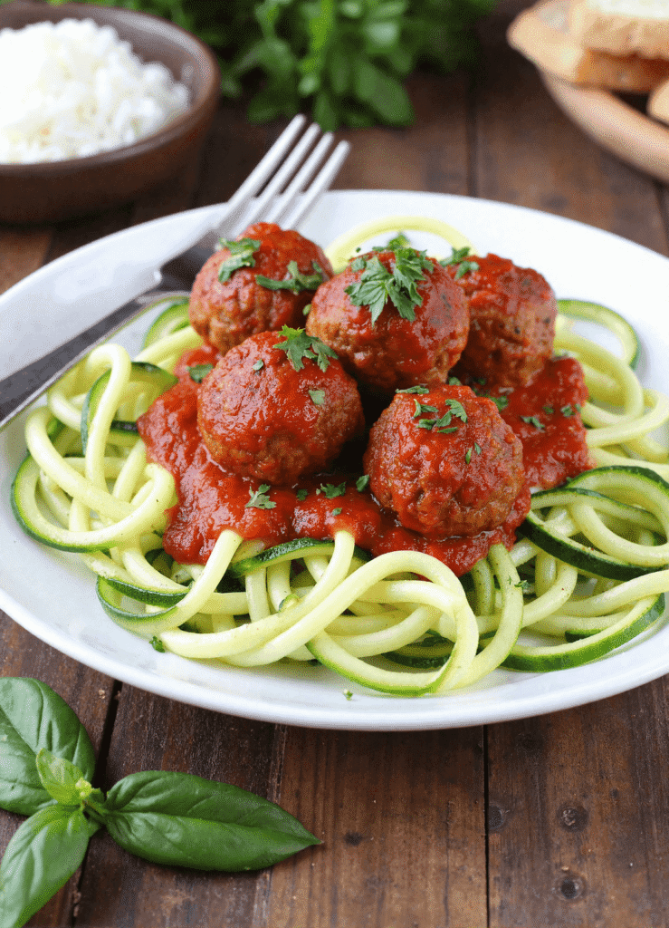 Golden-brown turkey meatballs on zucchini noodles topped with tomato sauce and chopped parsley.
