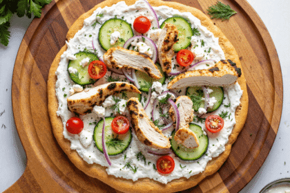 Whole flatbread pizza topped with tzatziki sauce, grilled chicken, cucumbers, tomatoes, red onion, and fresh herbs.