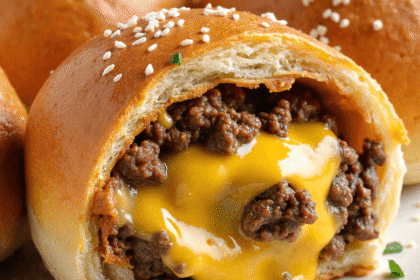Close-up of baked cheeseburger bomb filled with gooey melted cheese and seasoned ground beef, topped with sesame seeds and parsley.