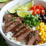 Cilantro lime steak bowl featuring sliced steak over rice with lime wedges, corn, black beans, diced tomato, and fresh cilantro for an easy Tex-Mex meal prep dish.