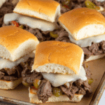 Close-up of Philly cheesesteak sliders with shaved beef, melted provolone, onions, and peppers on a sheet pan