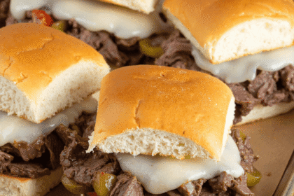 Close-up of Philly cheesesteak sliders with shaved beef, melted provolone, onions, and peppers on a sheet pan