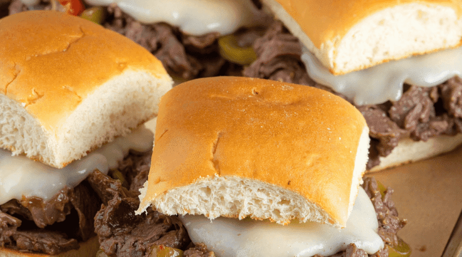 Close-up of Philly cheesesteak sliders with shaved beef, melted provolone, onions, and peppers on a sheet pan