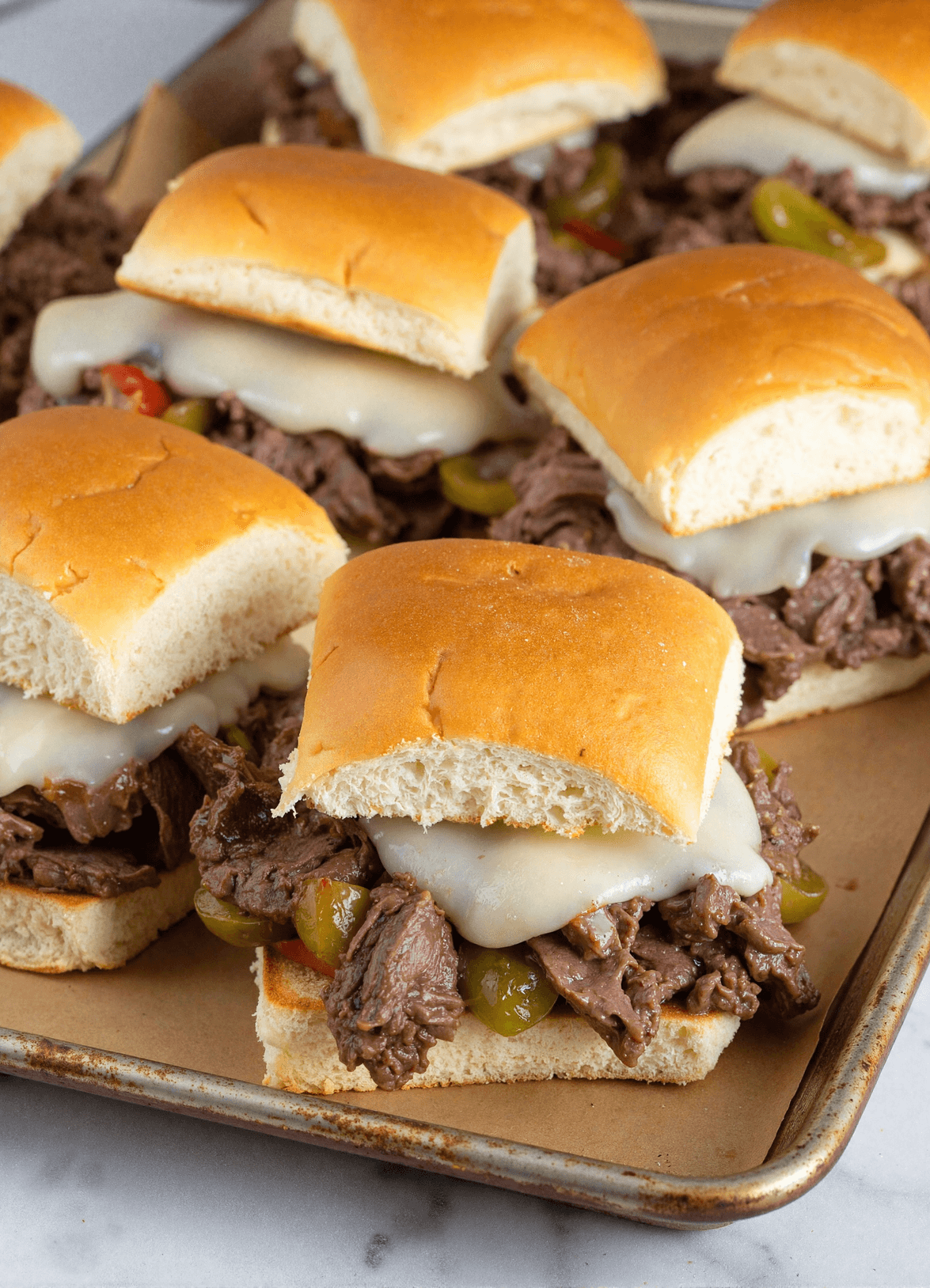 Close-up of Philly cheesesteak sliders with shaved beef, melted provolone, onions, and peppers on a sheet pan