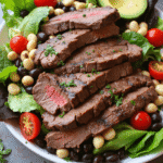 Grilled steak slices served over a vibrant green salad with black beans, cherry tomatoes, avocado slices, and red onion.